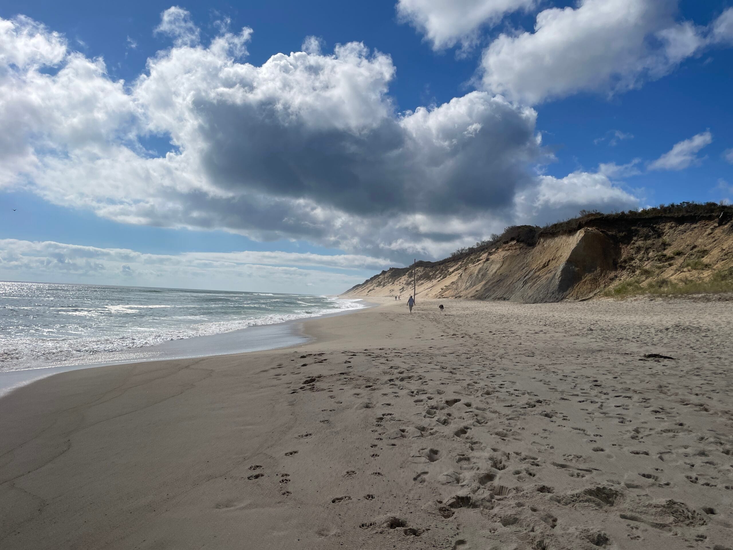 An ocean beach with sand dunes behind it and a partly cloudy sky above it.