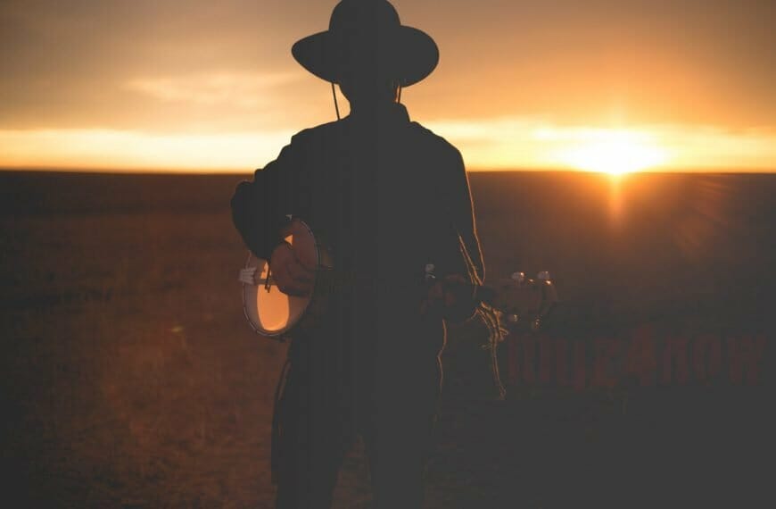 Someone with a wide-brimmed hat holding a banjo in the sunset - photo by Priscilla Du Preez