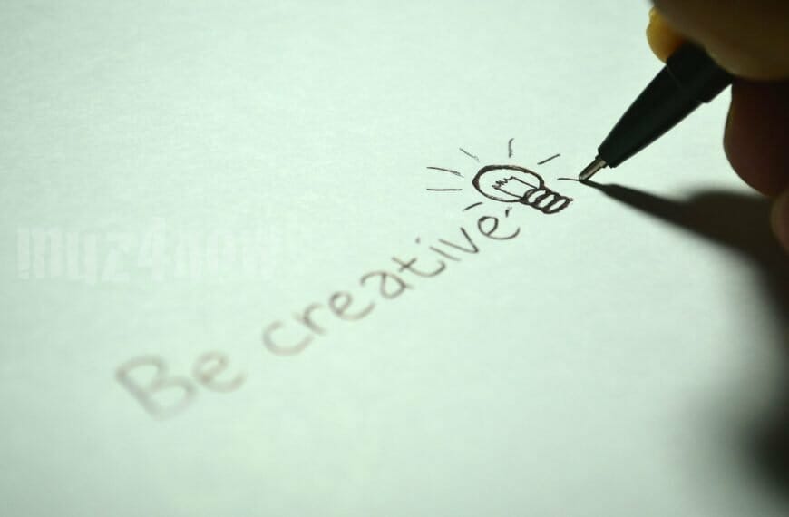 A hand with a pen writing "Be creative"