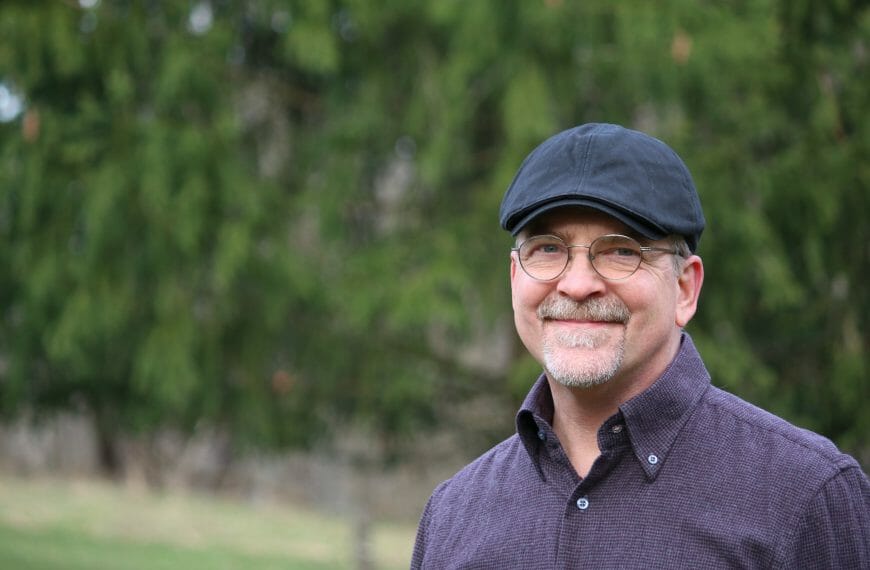 Stan Stewart smiles while wearing a blue cap in a forest