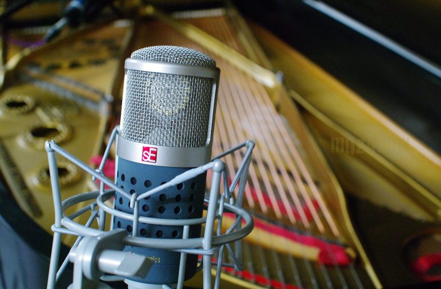 The image focuses on a large condenser microphone in front of a piano soundboard.