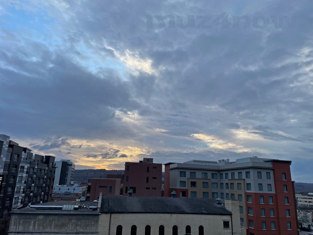 The sun barely peeks through gray clouds above a few high-rise buildings.