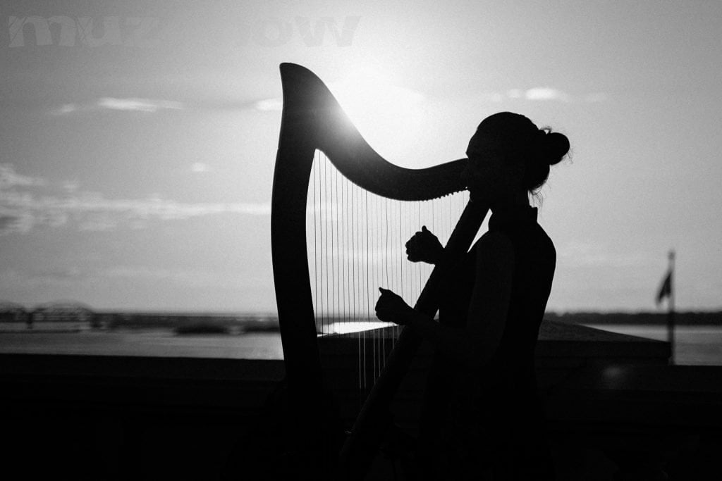 The silhouette of a harpist playing a harp as the sun sets behind her.