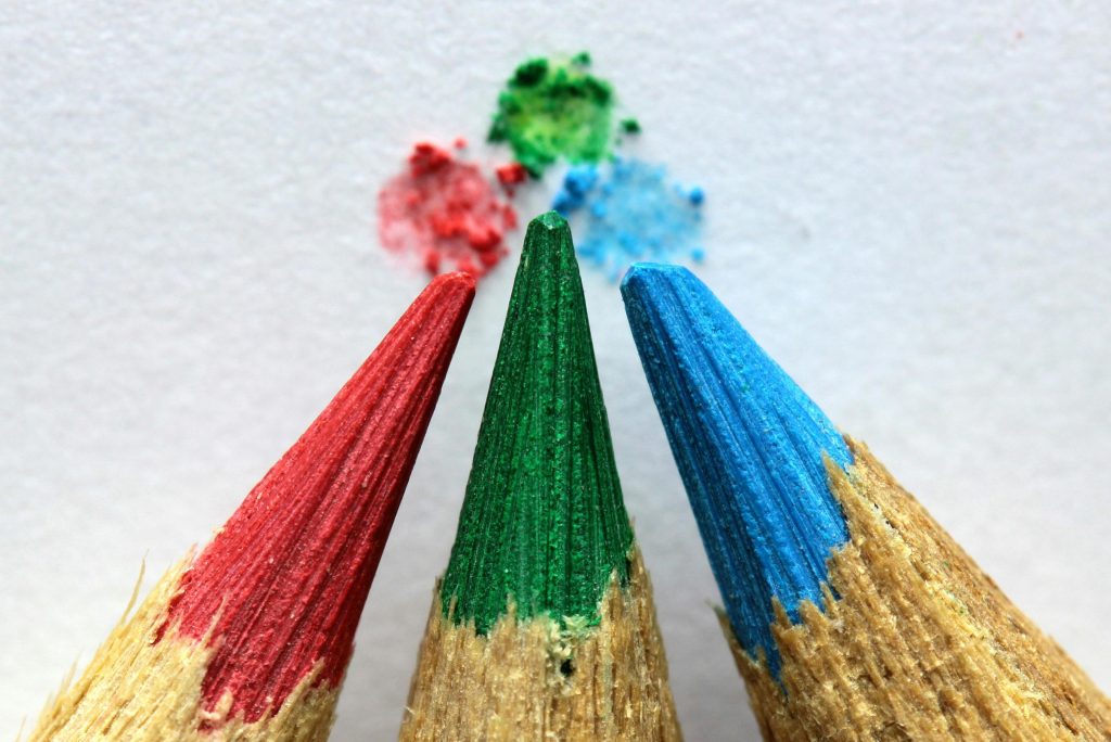 A red, green, and blue pencil with tiny blotch of each color on a paper background.