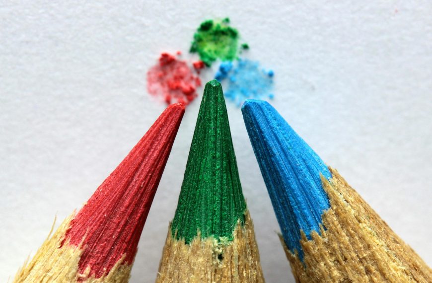 A red, green, and blue pencil with tiny blotch of each color on a paper background.