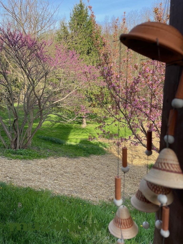 Recovery Bells - a set of ceramic bells hangs on a post with a bright colored garden behind it.