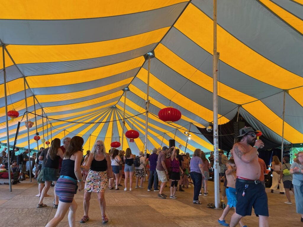 People laughing and dancing in a big yellow and gray tent at Grassroots music festival.