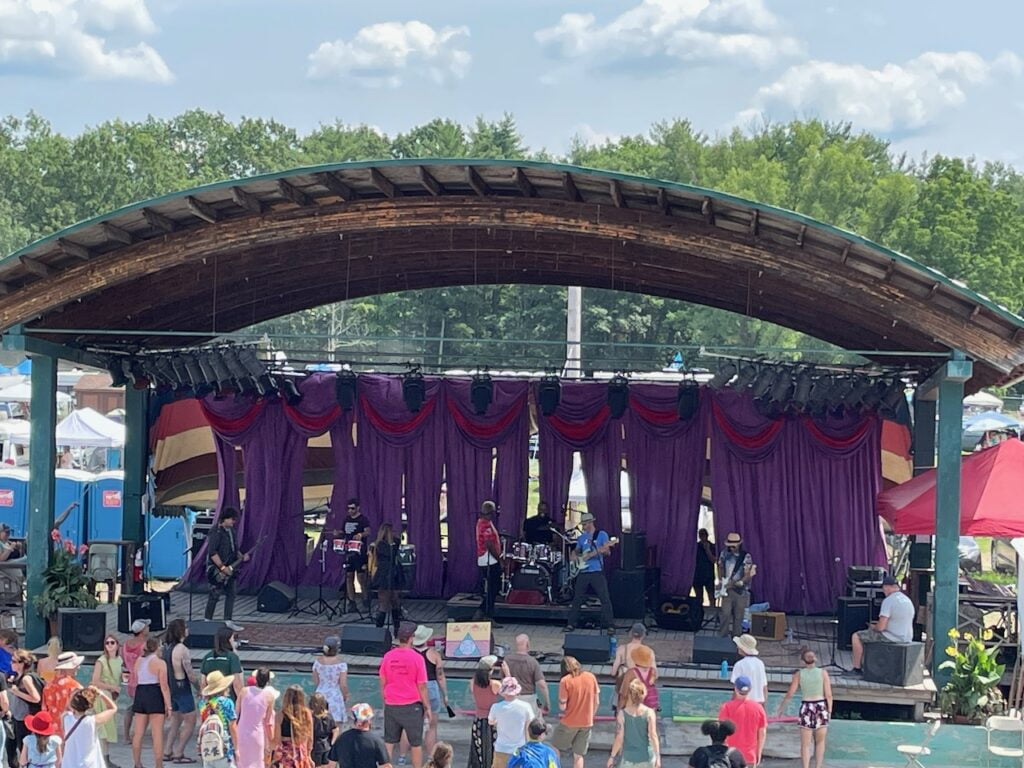 A funk band plays a concert in a big, outdoor stage.