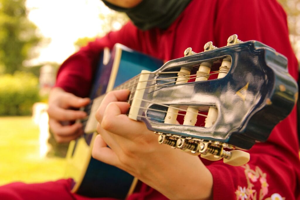 A Muslim woman wearing a red garment is playing a classical guitar.