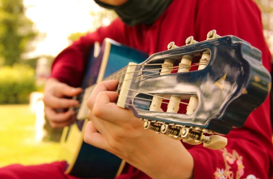 A Muslim woman wearing a red garment is playing a classical guitar.