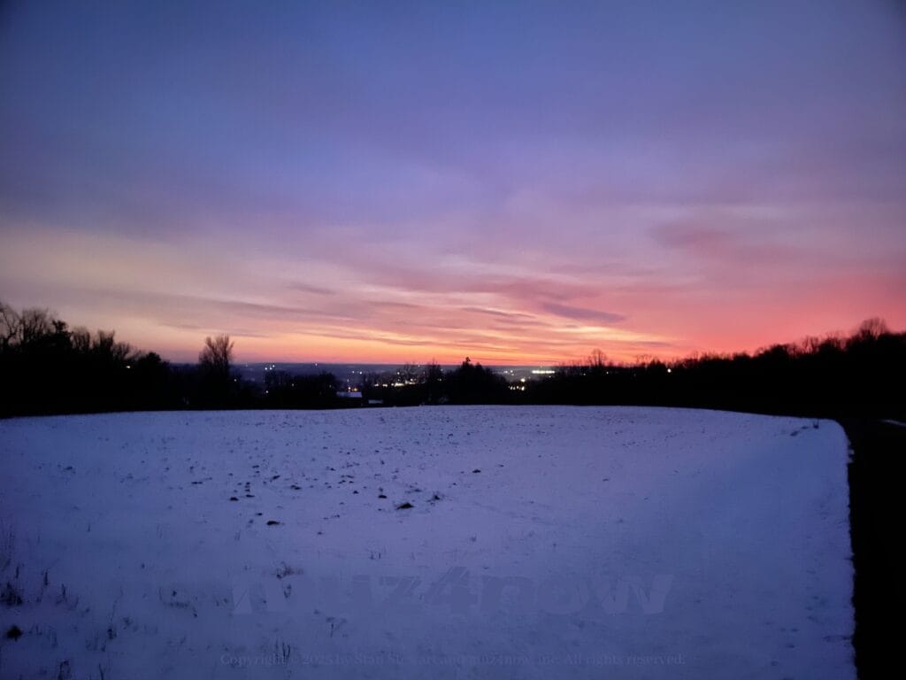Ready for beauty? Here's a red, orange, and yellow hue on the horizon as the sun rises behind the clouds. The ground is covered with snow.