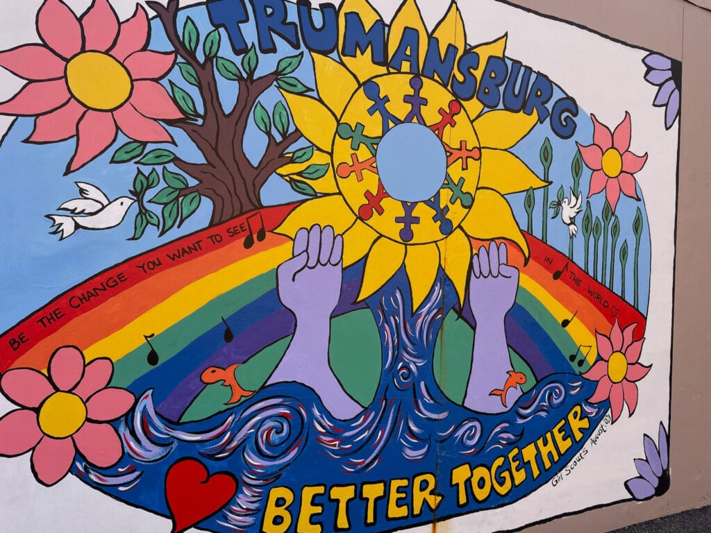 A brightly colored street painting of flowers, hearts, hands, waves, a stylized sun, and a rainbow. At the bottom is written "better together".