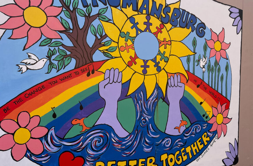 A brightly colored street painting of flowers, hearts, hands, waves, a stylized sun, and a rainbow. At the bottom is written "better together".