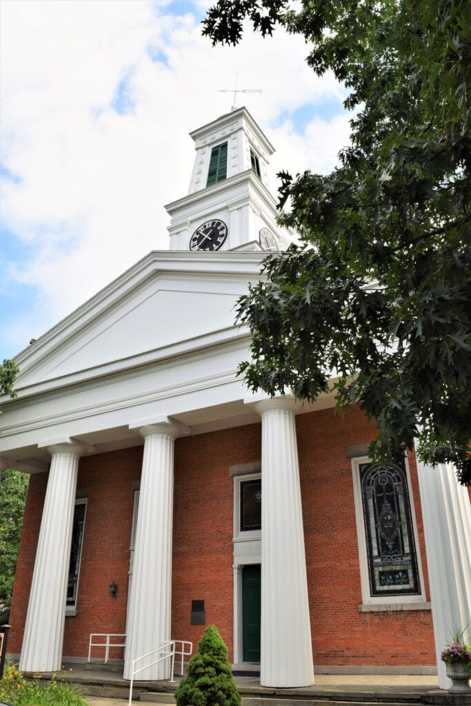 A church steeple with a clock on it above a brick building with columns holding up the roof.