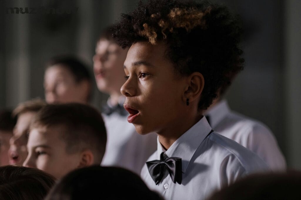 A children's choir with several members singing. The chorister in the foreground is wearing a black bowtie on an off-white shirt.
The photo is by cottonbro via pexels. https://www.pexels.com/@cottonbro/