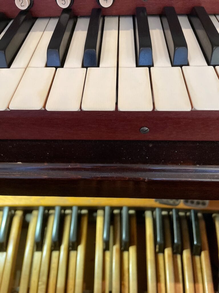 A few white and black keys on the bottom manual of a pipe organ. Below this keyboard and slightly out of focus is the center of the pedalboard for the organ.