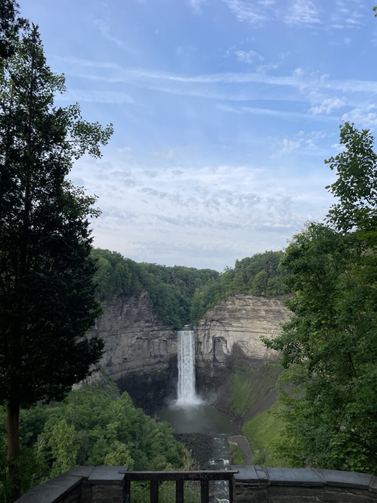 Beyond trees and railing is a tall waterfall coming down a rock wall.