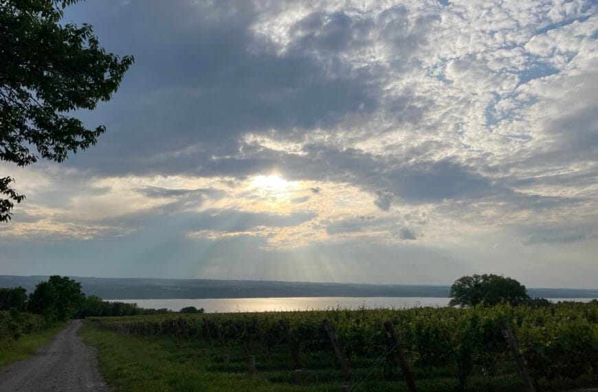 The setting sun shines rays of light downward through heavy cloud cover above a lake.