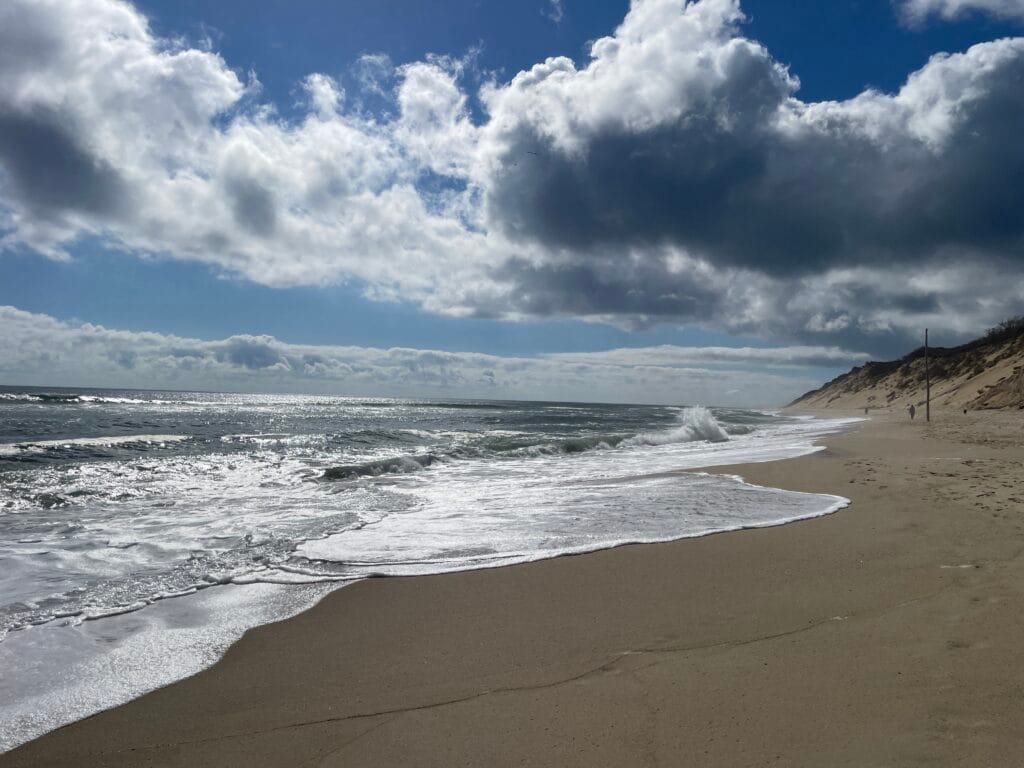 Ocean waves coming on to a sandy beach. The sky is half filled with fluffy clouds.