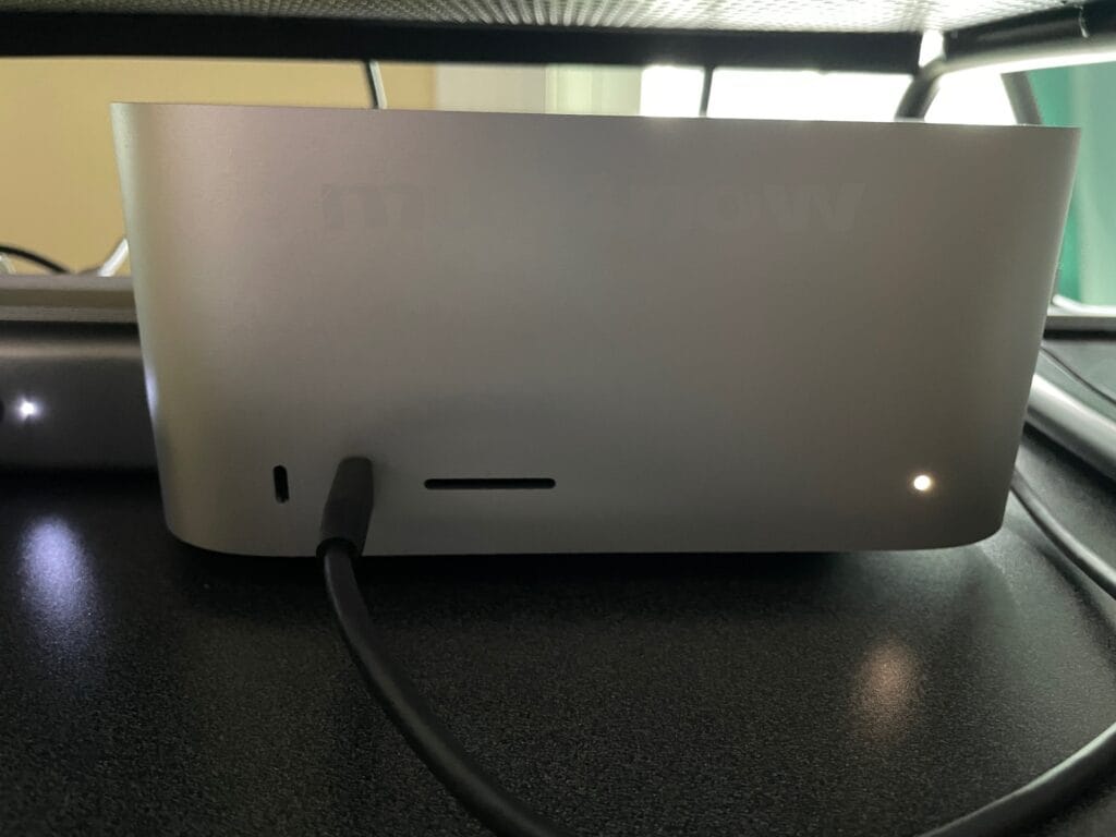 An Apple Mac Studio computer is basically a rectangular box. This one is powered on as indicated by a white light at the bottom right of the rectangle.
