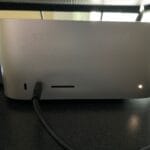 An Apple Mac Studio computer is basically a rectangular box. This one is powered on as indicated by a white light at the bottom right of the rectangle.
