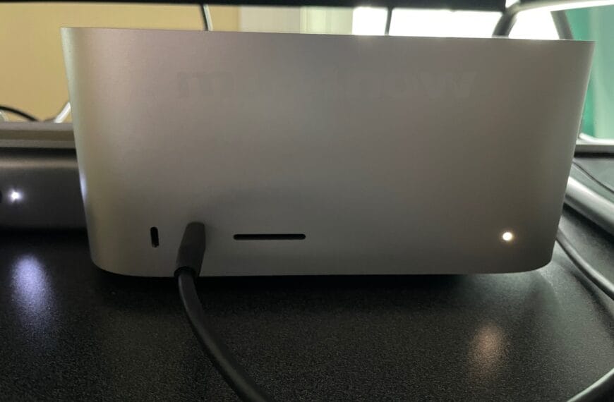 An Apple Mac Studio computer is basically a rectangular box. This one is powered on as indicated by a white light at the bottom right of the rectangle.