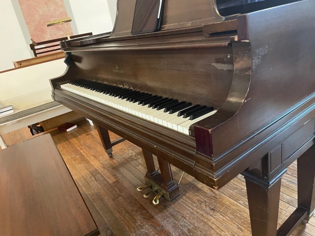 The keyboard of a grand piano with the bench and three pedals under it. The music stand above the keyboard is open with an iPad on it.