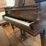 The keyboard of a grand piano with the bench and three pedals under it. The music stand above the keyboard is open with an iPad on it.