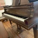 The keyboard of a grand piano with the bench and three pedals under it. The music stand above the keyboard is open with an iPad on it.