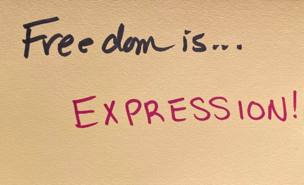 "Freedom is... EXPRESSION!" written in felt-tip marker on a beige index card. Written as a prompt for a piano improvisation concert.
