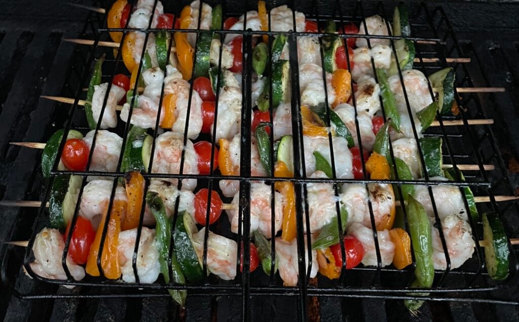 A grill with skewers of vegetables and shrimp cooking.