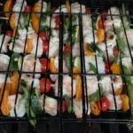 A grill with skewers of vegetables and shrimp cooking.