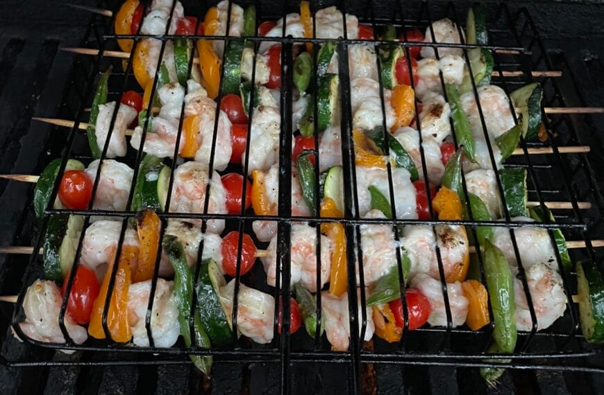 A grill with skewers of vegetables and shrimp cooking.