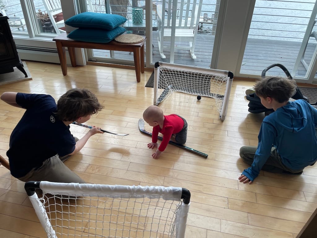 Three young children are on a wooden floor playing with miniature hockey sticks and goals. Having grandchildren is one of the beautiful changes in my life.