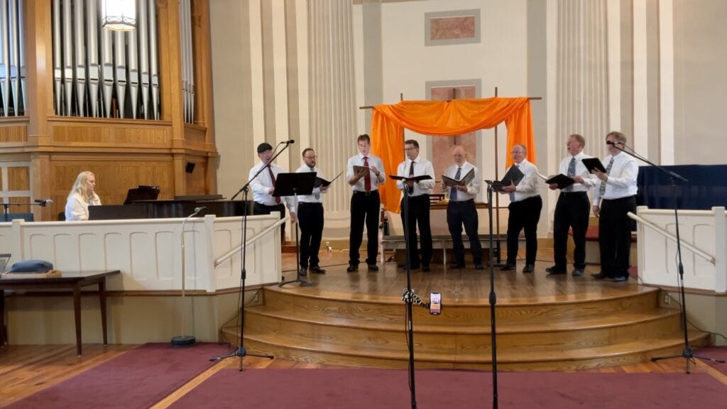 Eight singers and a pianist on a stage performing. No blahs here.