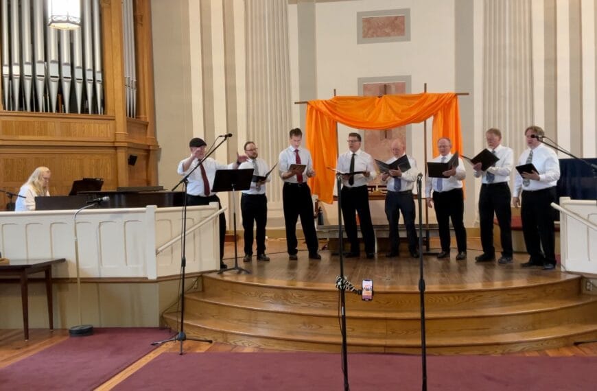 A group of 8 singers --the one on the far left is conducting -- and a pianist performing. Hopefully they don't experience the blahs after the gig.