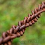 A rusty chain with blurry green background is symbolic of connection. Original photo by https://pixabay.com/users/analogicus-8164369/