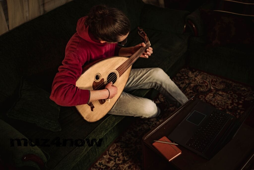 Someone seated on a couch, playing taqsim on an oud. They are wearing a red sweatshirt and white pants. Their hair is black and tied back. The perspective of the image is from above. The photo is by https://www.pexels.com/@abedalbaset/