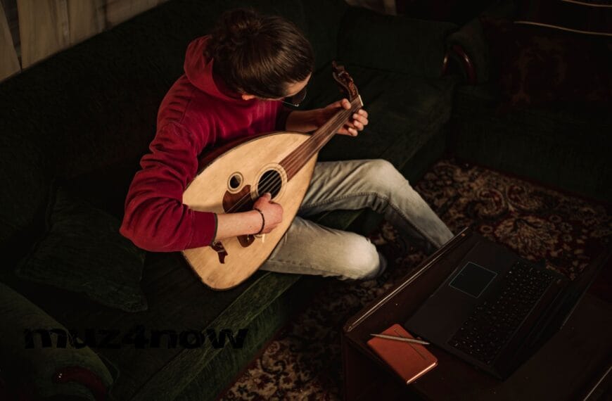 Someone seated on a couch, playing taqsim on an oud. They are wearing a red sweatshirt and white pants. Their hair is black and tied back. The perspective of the image is from above. The photo is by https://www.pexels.com/@abedalbaset/