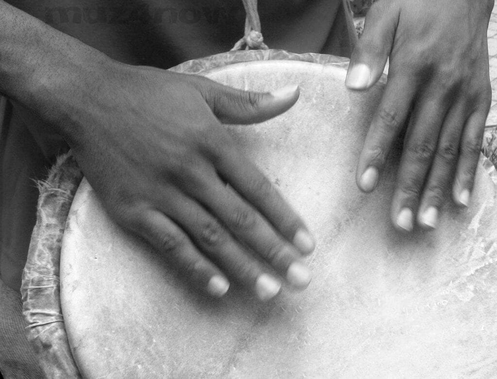 Someone has both of their hands on a large drum head. Drums and other instruments vary with our culture.