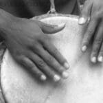 Someone has both of their hands on a large drum head. Drums and other instruments vary with our culture.