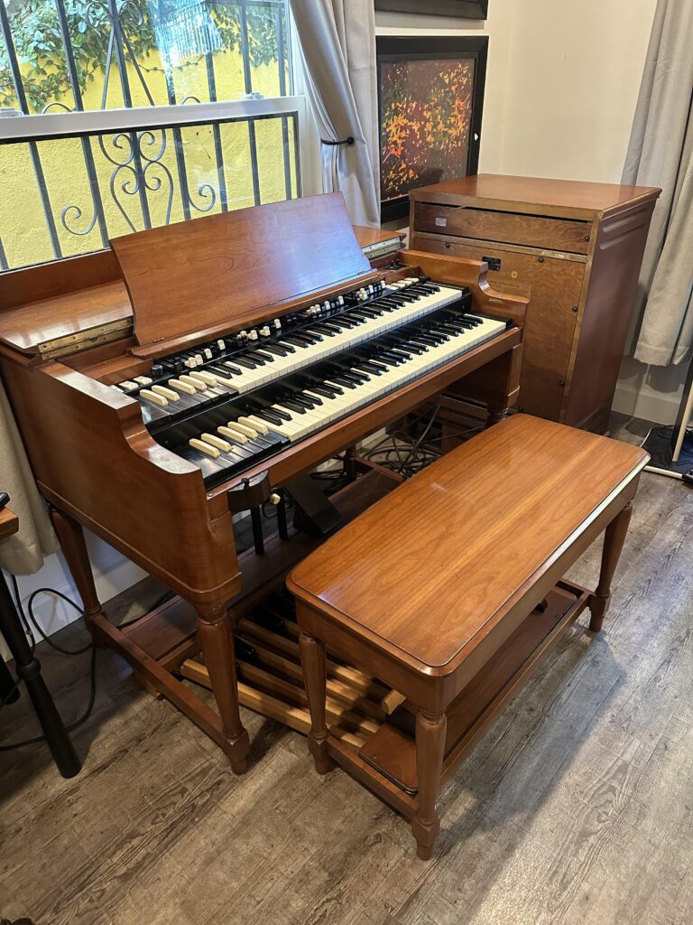 A Hammond B3 with wooden bench and Leslie speaker is next to a window. Found at https://www.reddit.com/r/hammondorgan/comments/186f7l6/my_new_acquisition_today_a_pristine_b3_with/