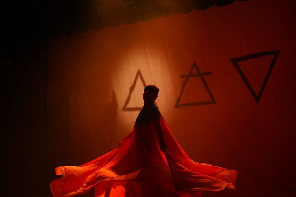A dancer in layers of red chiffon moves in front of symbols for the elements fire, air, and earth