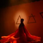 A dancer in layers of red chiffon moves in front of symbols for the elements fire, air, and earth