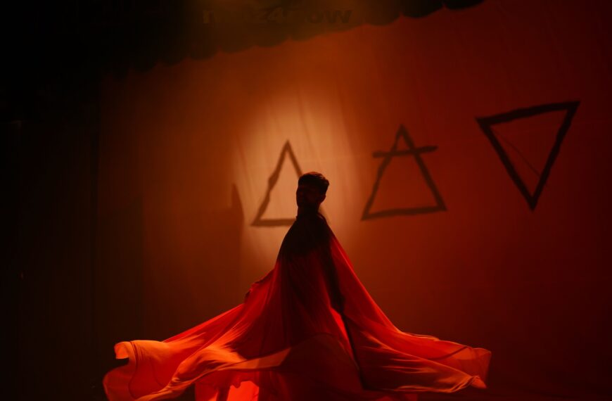 A dancer in layers of red chiffon moves in front of symbols for the elements fire, air, and earth